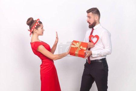 Photo for Portrait of shocked sad woman showing stop gesture to man with present box and red heart in hands, female saying no, refuse a gift. Indoor studio shot isolated on gray background. - Royalty Free Image