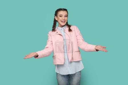 Téléchargez les photos : Portrait d'une adolescente amicale avec des tresses portant une veste rose debout les mains ouvertes, partageant avec quelqu'un gratuitement. Studio intérieur tourné isolé sur fond vert. - en image libre de droit