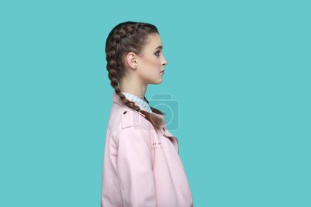 Photo for Side view portrait of strict bossy young teenager girl with braids wearing pink jacket looking ahead with serious facial expression, being in bad mood. Indoor studio shot isolated on green background. - Royalty Free Image