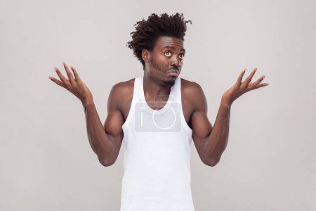 Photo for I don`t know this. Portrait of confused puzzled man with Afro hairstyle feels uncertain as can`t find right way, wearing white T-shirt. Indoor studio shot isolated on gray background. - Royalty Free Image