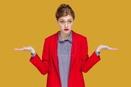 Photo for I do not know. Puzzled uncertain woman with red lips standing and spreads hands, looking at camera with confused expression, wearing red jacket. Indoor studio shot isolated on yellow background. - Royalty Free Image