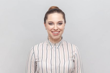 Photo for Portrait of attractive joyful cheerful woman wearing striped shirt looking at camera with toothy smile, being in good mood, expressing positiveness. Indoor studio shot isolated on gray background. - Royalty Free Image