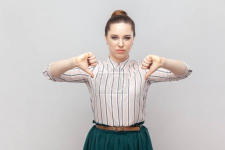Photo for Portrait of dissatisfied displeased attractive woman wearing striped shirt and green skirt standing showing dislike gesture, looks unhappy. Indoor studio shot isolated on gray background. - Royalty Free Image