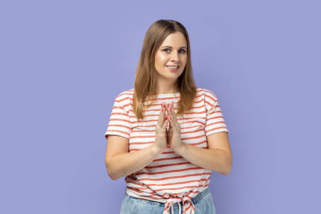 Photo for Cunning blond woman wearing striped T-shirt gesticulating and thinking over devious sly plan of revenge, scheming and conspiring villain plan. Indoor studio shot isolated on purple background. - Royalty Free Image