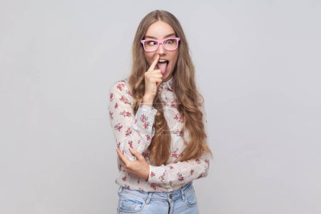 Photo for Portrait of funny woman in glasses with wavy blond hair putting finger into his nose, fooling around, bad habits, disrespectful behavior. Indoor studio shot isolated on gray background. - Royalty Free Image