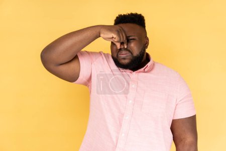 Photo for What is a bad small? Portrait of man pinching nose, stop breathing bad odor, disgusted by smell of farting, expressing repulsion, gross. Indoor studio shot isolated on yellow background. - Royalty Free Image