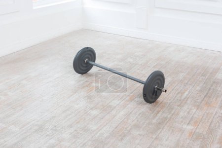 Photo for Heavy barbell on floor in gym on white wall background. Sport equipment. Indoor studio shot. - Royalty Free Image