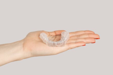 Primer plano de la mano de la mujer que muestra alineadores cosméticos de ortodoncia invisible. Estudio interior plano aislado sobre fondo gris.