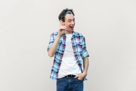 Photo for Optimistic glad excited man makes gesture with fore finger upwards, having great idea, smiling, wearing blue checkered shirt and headband. Indoor studio shot isolated on gray background. - Royalty Free Image