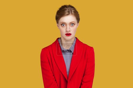 Photo for Portrait of shocked scared frighten woman with red lips standing looking at camera with big eyes, sees something scary, wearing red jacket. Indoor studio shot isolated on yellow background. - Royalty Free Image