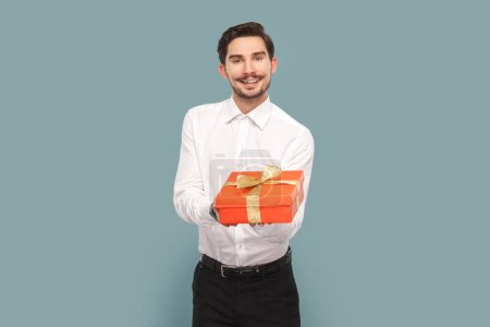 Photo for Portrait of friendly positive optimistic man with mustache giving red present box, congratulating with holiday, wearing Indoor studio shot isolated on light blue background. - Royalty Free Image