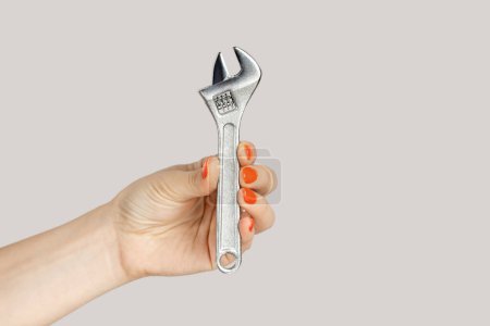 Photo for Closeup of woman hand holding adjustable wrench, mechanic and repairman tools and instruments. Indoor studio shot isolated on gray background. - Royalty Free Image