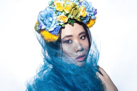 Photo for Closeup portrait of sensual beautiful young adult woman with floral hat and blue veil, looking at camera with serious expression. Indoor studio shot isolated on gray background, - Royalty Free Image