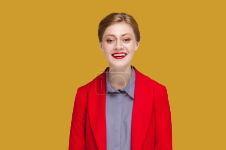 Photo for Portrait of happy satisfied woman with red lips standing looking at camera with toothy smile, expressing happiness, wearing red jacket. Indoor studio shot isolated on yellow background. - Royalty Free Image