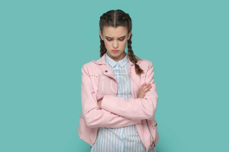 Téléchargez les photos : Portrait d'adolescente triste offensée avec des tresses portant une veste rose debout avec la main vers le bas, étant de mauvaise humeur, se disputant avec quelqu'un. Studio intérieur tourné isolé sur fond vert. - en image libre de droit