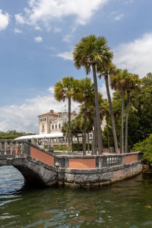 Foto de Miami, Florida - 25 de agosto de 2023: Puente de estilo veneciano y palmeras en Vizcaya Museum & Garden en Miami, Florida. - Imagen libre de derechos