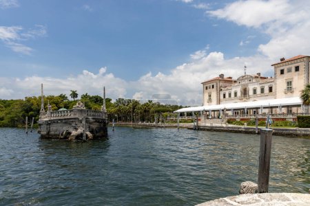 Foto de Miami, Florida - 25 de agosto de 2023: Barcaza de rompeolas de piedra y magnífica mansión Vizcaya en la bahía de Vizcaya bajo el cielo azul. - Imagen libre de derechos