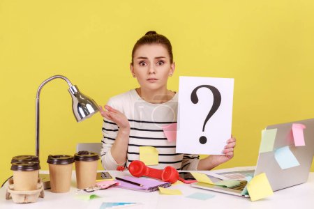 Photo for Portrait of shocked astonished woman looking at camera, holding paper with question mark, thinks about tasks, covered with sticky notes. Indoor studio studio shot isolated on yellow background. - Royalty Free Image