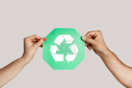 Photo for Closeup of woman and man hand holding green recycling sign, ecological icon, environment protection. Indoor studio shot isolated on gray background. - Royalty Free Image