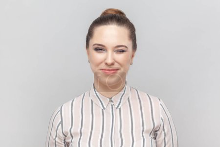 Photo for Portrait of beautiful playful woman wearing striped shirt standing looking at camera and winking, flirting with her boyfriend, smiling happily. Indoor studio shot isolated on gray background. - Royalty Free Image