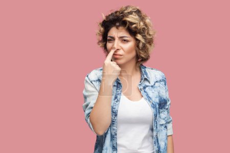 Photo for You are liar. Portrait of serious beautiful young adult woman with curly hairstyle wearing blue shirt standing pointing at her nose with finger. Indoor studio shot isolated on pink background. - Royalty Free Image