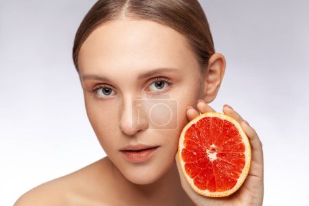 Photo for Closeup portrait of beautiful woman with perfect skin model looking at camera holding half of grapefruit. Indoor studio shot isolated over gray background. - Royalty Free Image
