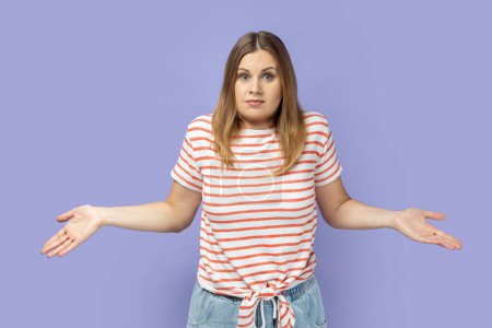 Photo for I don't know. Uncertain woman standing with confused puzzled emotion, spreading hands in questioning gesture, expressing embarrassment and doubts. Indoor studio shot isolated on purple background. - Royalty Free Image