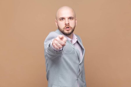 Photo for Man having mad expression pointing his finger at camera, looking angrily and frowning as if accusing or blaming you for mistake, wearing gray jacket. Indoor studio shot isolated on brown background. - Royalty Free Image