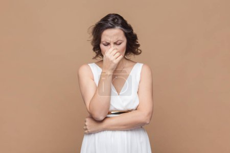 Photo for Portrait of sad crying disappointed middle aged woman with wavy hair looking unhappy crying, having problems, wearing white dress. Indoor studio shot isolated on light brown background. - Royalty Free Image