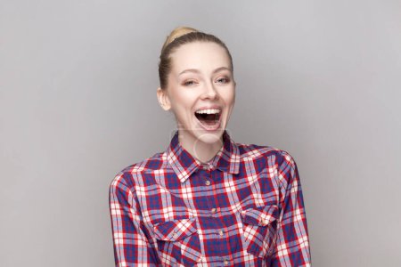 Photo for Portrait of joyful cheerful extremely happy woman with bun hairstyle hearing nice joke, laughing out loud, wearing checkered shirt. Indoor studio shot isolated on gray background. - Royalty Free Image