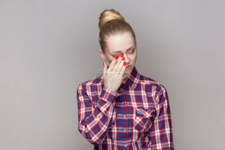 Photo for Portrait of despair sad stressed woman with bun hairstyle crying, having problems, wiping her tears, being in depression, wearing checkered shirt. Indoor studio shot isolated on gray background. - Royalty Free Image