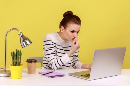 Photo for Bossy annoyed woman touching nose, doing liar gesture, looking with suspicion at laptop screen, having video call, online conference. Indoor studio studio shot isolated on yellow background. - Royalty Free Image