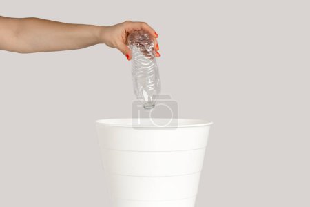 Photo for Closeup of woman hand throwing away empty plastic bottle, saving environment, recycle. Indoor studio shot isolated on gray background. - Royalty Free Image