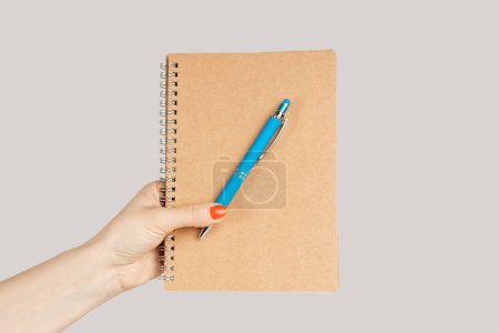 Photo for Closeup of woman hand showing organizer withemptycover and pen, copy space for advertisement. Indoor studio shot isolated on gray background. - Royalty Free Image