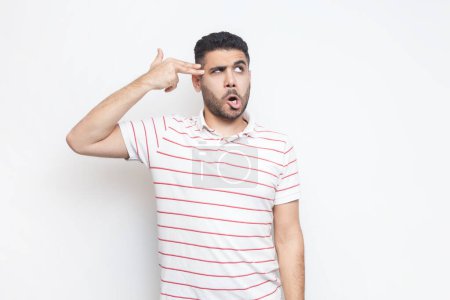 Photo for Portrait of funny crazy handsome bearded man wearing striped t-shirt standing with fingers near head, making suicide gesture, looking away. Indoor studio shot isolated on gray background. - Royalty Free Image