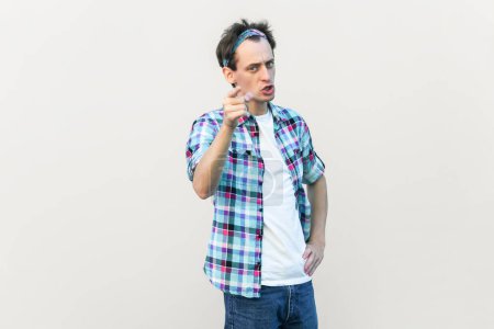 Photo for I told you. Displeased man warns someone, raises fore finger with strict expression, shows admonishing gesture, wearing checkered shirt and headband. Indoor studio shot isolated on gray background. - Royalty Free Image