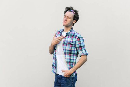 Photo for This is me. Proud man points at himself, stands self confident, feels successful of his own achievement, wearing blue checkered shirt and headband. Indoor studio shot isolated on gray background. - Royalty Free Image