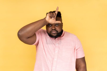 Photo for Portrait of upset disappointed man wearing pink shirt showing looser gesture with hand on forehead, having financial and business problems. Indoor studio shot isolated on yellow background. - Royalty Free Image