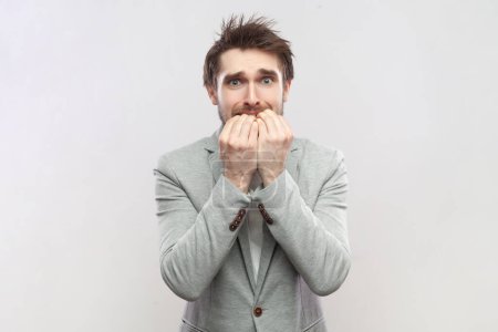 Photo for Portrait of nervous worried attractive man biting his fingernails, looking at camera, having problems, looks scared, wearing grey suit and blue bow tie. Indoor studio shot isolated on gray background. - Royalty Free Image