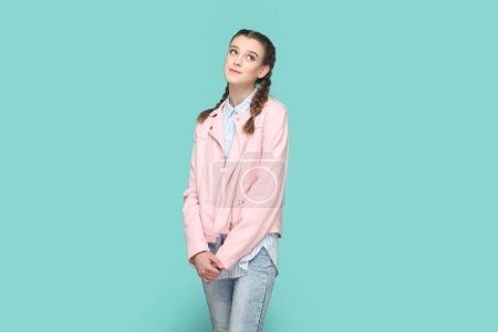 Téléchargez les photos : Portrait d'adolescente optimiste positive avec des tresses veste rose debout regardant loin rêvant à l'avenir sortir ensemble. Studio intérieur tourné isolé sur fond vert. - en image libre de droit