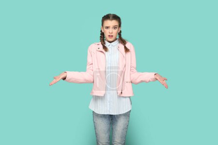 Photo for Portrait of confused angry teenager girl with braids wearing pink jacket standing with spread hands, looking at camera, asking what, don't understand. Indoor studio shot isolated on green background. - Royalty Free Image