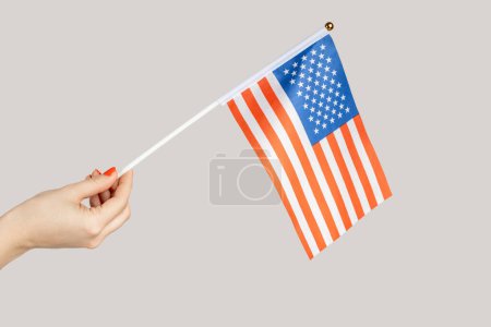 Foto de Primer plano de la mano de mujer mostrando bandera americana, viajando a Estados Unidos, inmigración. Estudio interior plano aislado sobre fondo gris. - Imagen libre de derechos