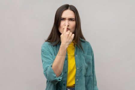 Photo for You are liar. Portrait of serious young woman with dark standing with finger on her nose and showing lie gesture, wearing casual style jacket. Indoor studio shot isolated on gray background. - Royalty Free Image