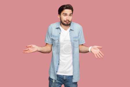 Photo for Portrait of unaware questioned man standing spreads palms, shrugs shoulders with perplexed expression, being indecisive, has no idea what happened. Indoor studio shot isolated on pink background. - Royalty Free Image