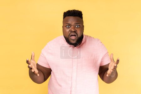 Photo for Portrait of annoyed stressed man wearing pink shirt asking what do you want and spreading hands, family quarrel, misunderstanding. Indoor studio shot isolated on yellow background. - Royalty Free Image