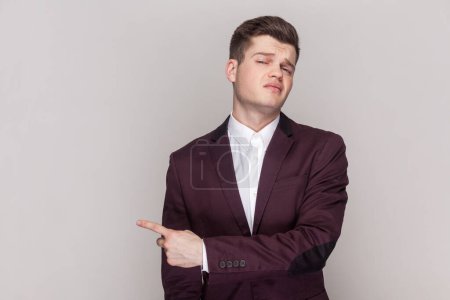 Photo for Portrait of annoyed handsome young man asking to leave him, showing exit, feeling betrayed and resentful, wearing violet suit and white shirt. Indoor studio shot isolated on grey background. - Royalty Free Image