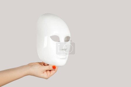 Photo for Closeup of woman hand showing white mysterious mask, hiding personality. Indoor studio shot isolated on gray background. - Royalty Free Image