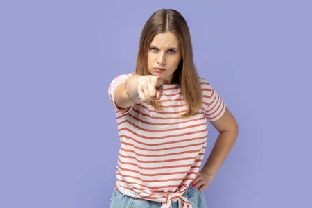 Photo for Hey you, be careful. Portrait of serious strict blond woman wearing striped T-shirt seriously pointing finger and looking at camera, warning.Indoor studio shot isolated on purple background. - Royalty Free Image