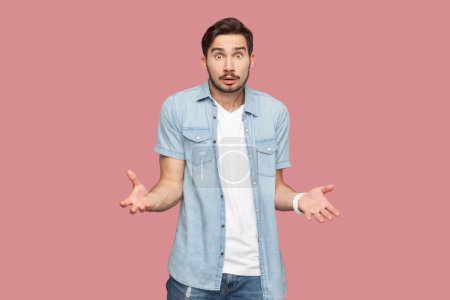 Photo for How could you. Annoyed indignant bearded man in blue casual style shirt spreads palms, looks angrily at camera quarrels with someone feels puzzled. Indoor studio shot isolated on pink background. - Royalty Free Image