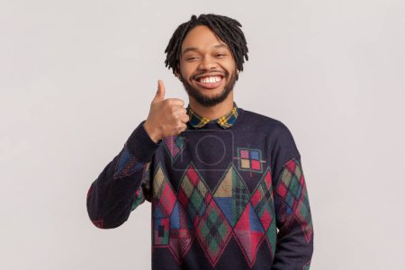 Photo for Portrait of smiling satisfied positive african-american man with dreadlocks and beard standing looking at camera, showing thumb up, good feedback. Indoor studio shot isolated on gray background. - Royalty Free Image